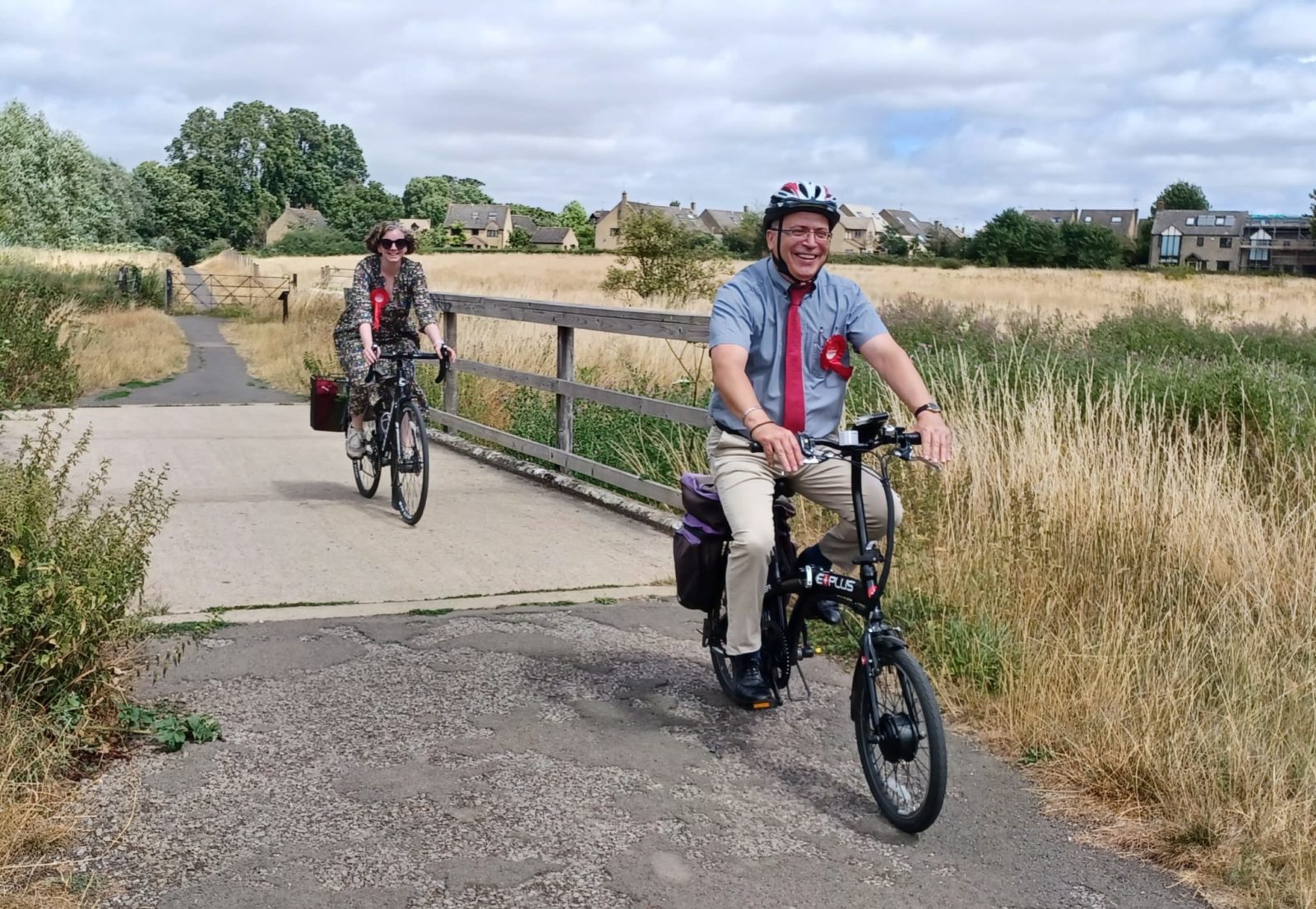 In the image, Andrew is cycling on Langel Common with Cllr Ruth Smith. In the background is the field recently purchased for the public by residents and West Oxfordshire District Council, to safeguard it from development and keep the common whole. The new council administration was delighted to be able to assist.